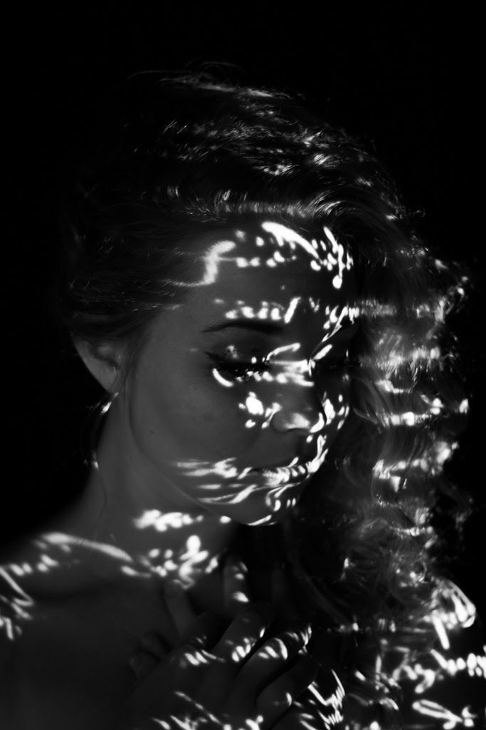 A woman in profile, her face and hair covered in scattered flecks of projected light.