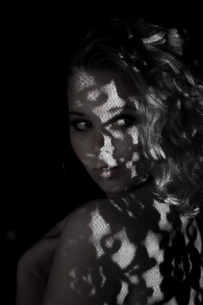 A woman looking back over her bare shoulder through a projected lace pattern.