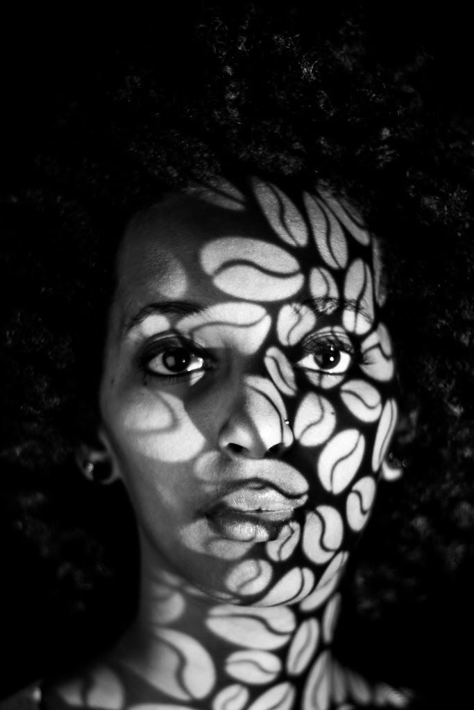 A woman facing the camera, her face covered in a projected pattern of leaf shapes.
